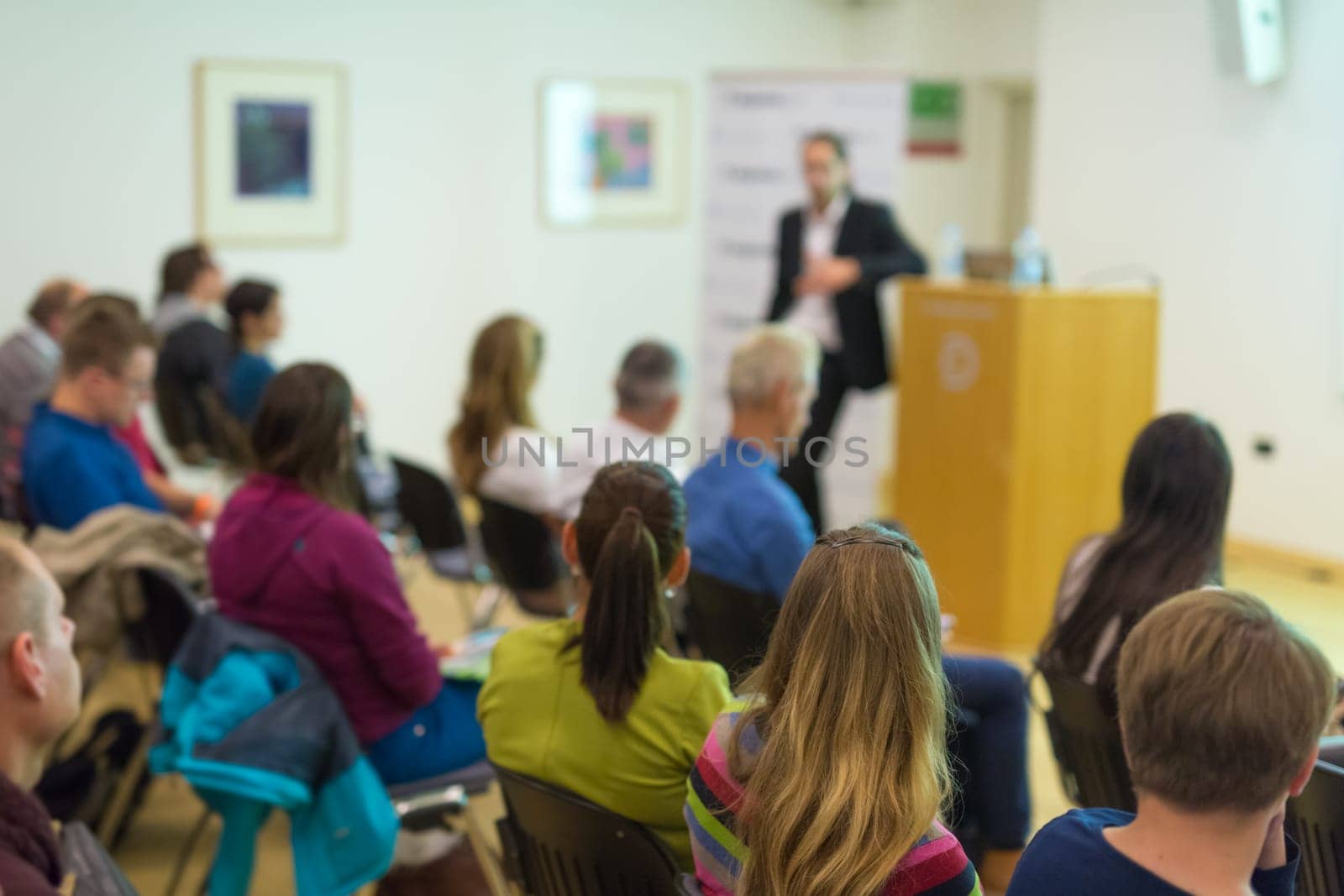 Speaker Giving a Talk at Business Meeting. Audience in the conference hall. Business and Entrepreneurship. Focus on unrecognizable people from rear.