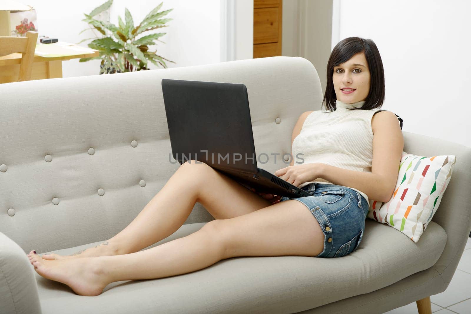 young brunette girl student lying on the couch with a laptop