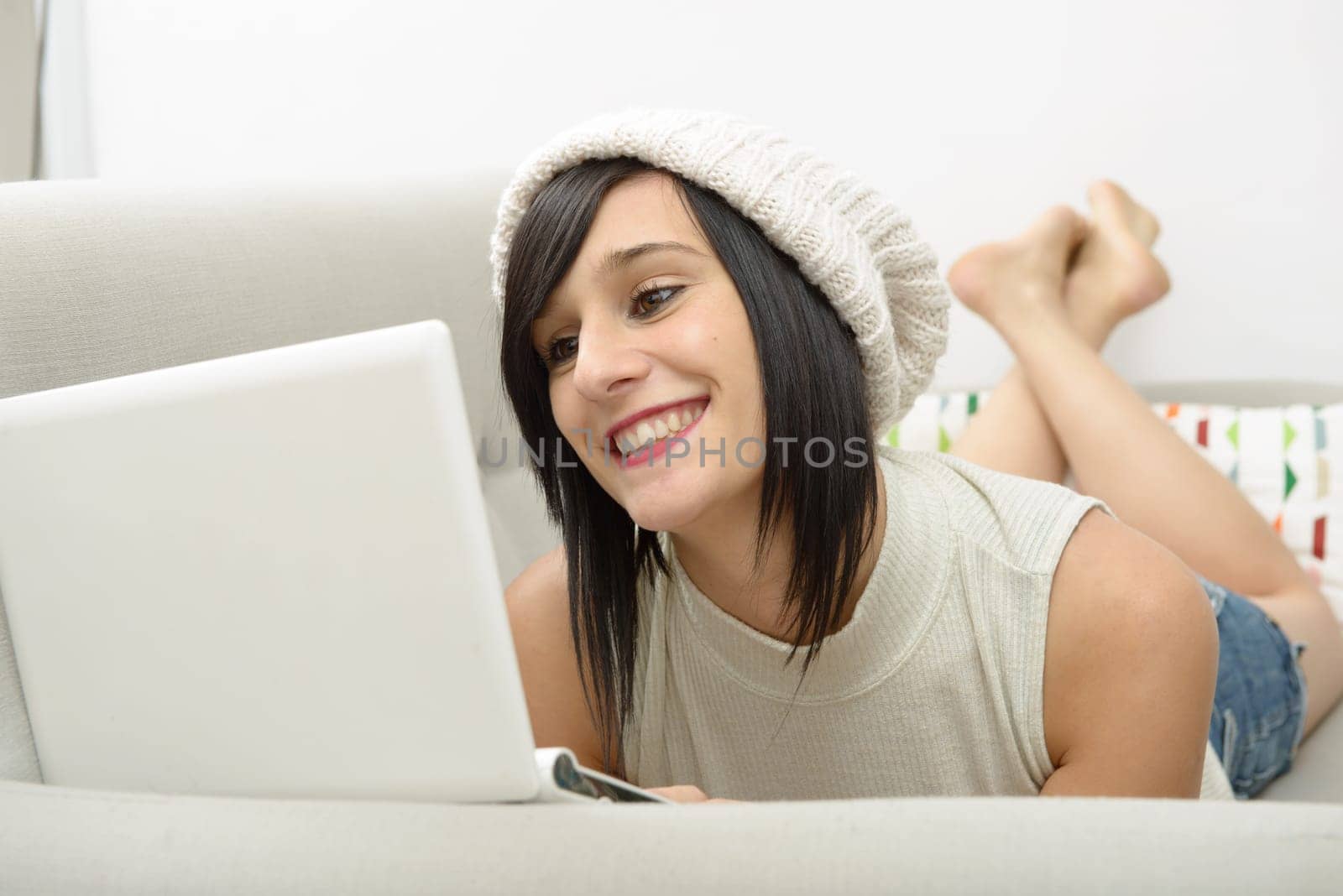 young brunette girl student lying on the couch with a laptop