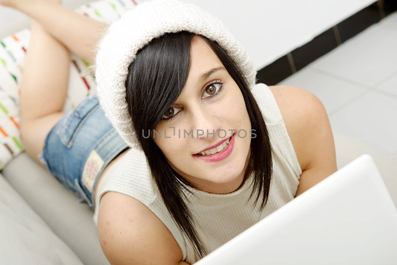 young brunette girl student lying on the couch with a laptop