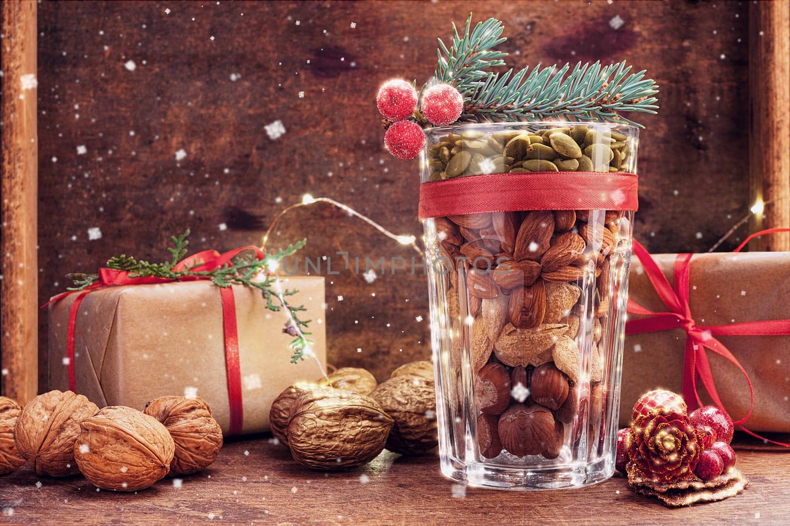 Christmas decoration glass with a variety of nuts on a wooden background with flying snow and copy space
