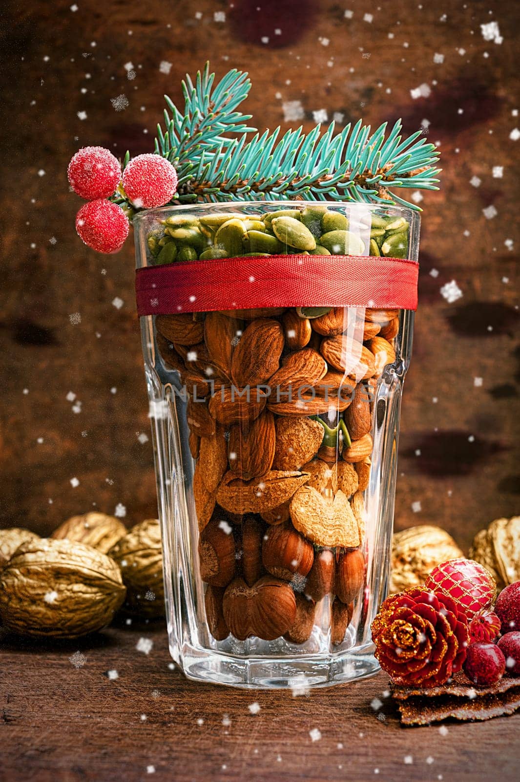 Christmas decoration glass with a variety of nuts on a wooden background with flying snow
