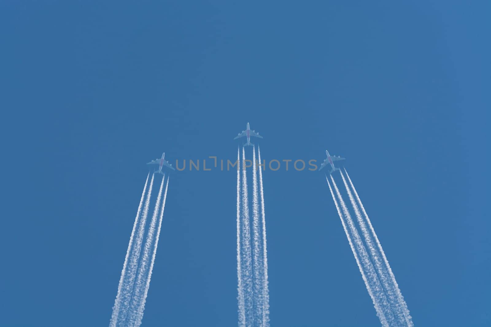 Three planes flying at high altitude. Contrails against a dark blue sky.