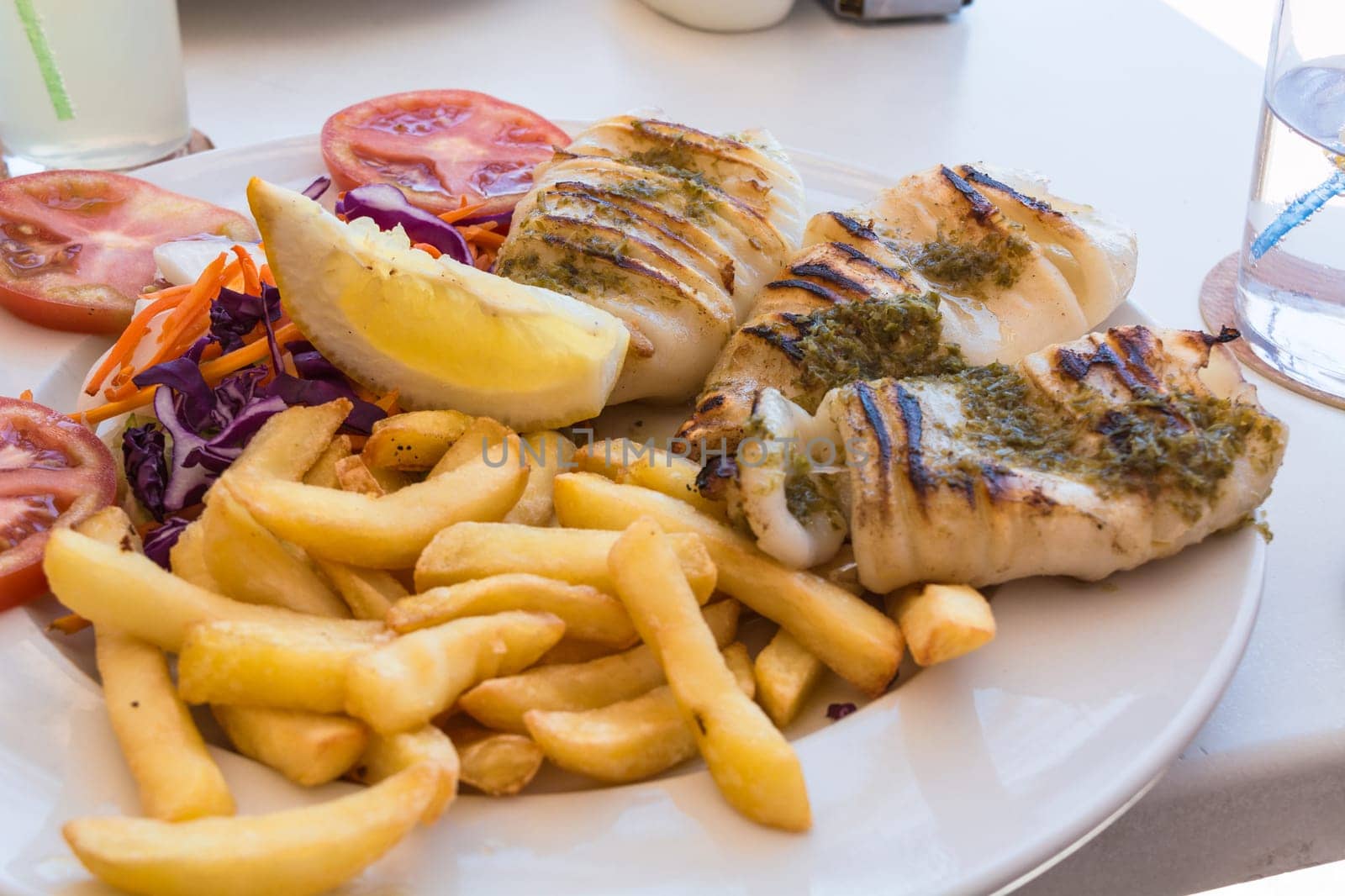 Grilled octopus. Grilled squid served with French fries and lemons and salad.