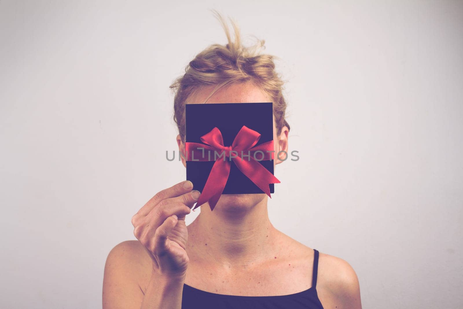 Portrait of a young Caucasian woman holding a black gift card with red ribbon in front of her face