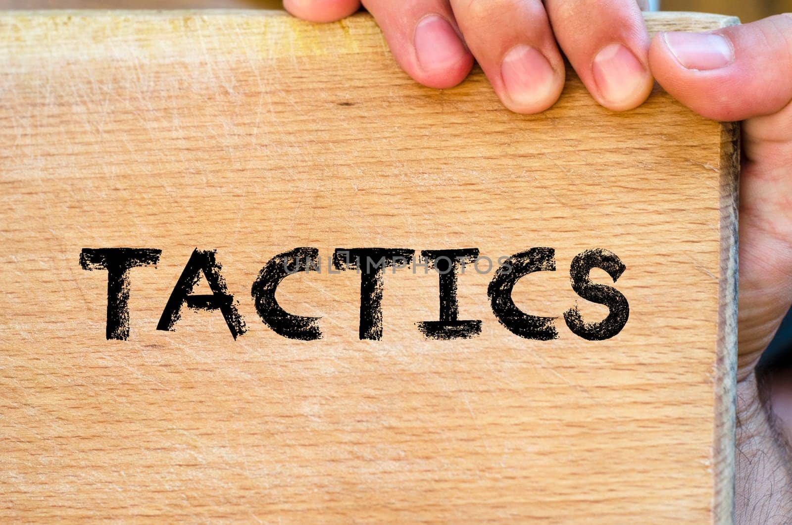 Human hand over wooden background and tactics text concept