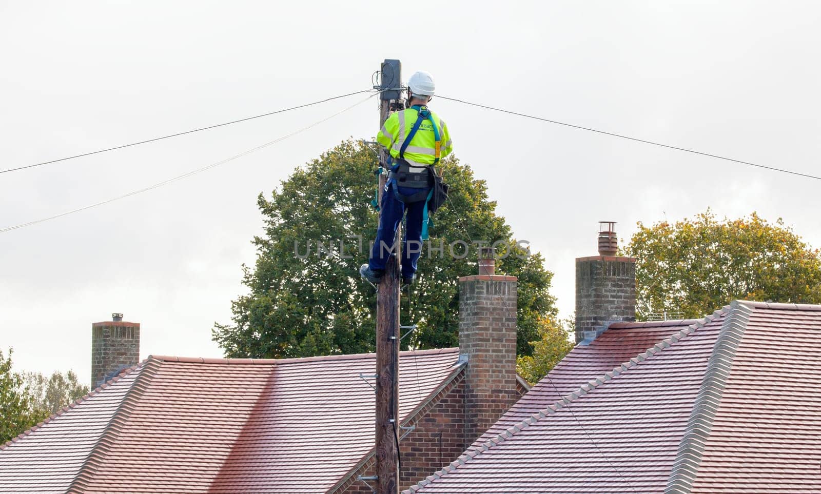 FAKENHAM, NORFOLK / UK - 10th OCTOBER 2016: Openreach BT engineer fixing cables up a pole. UK internet and telephone infrastructure provider at work providing internet and telephone services to rural locations