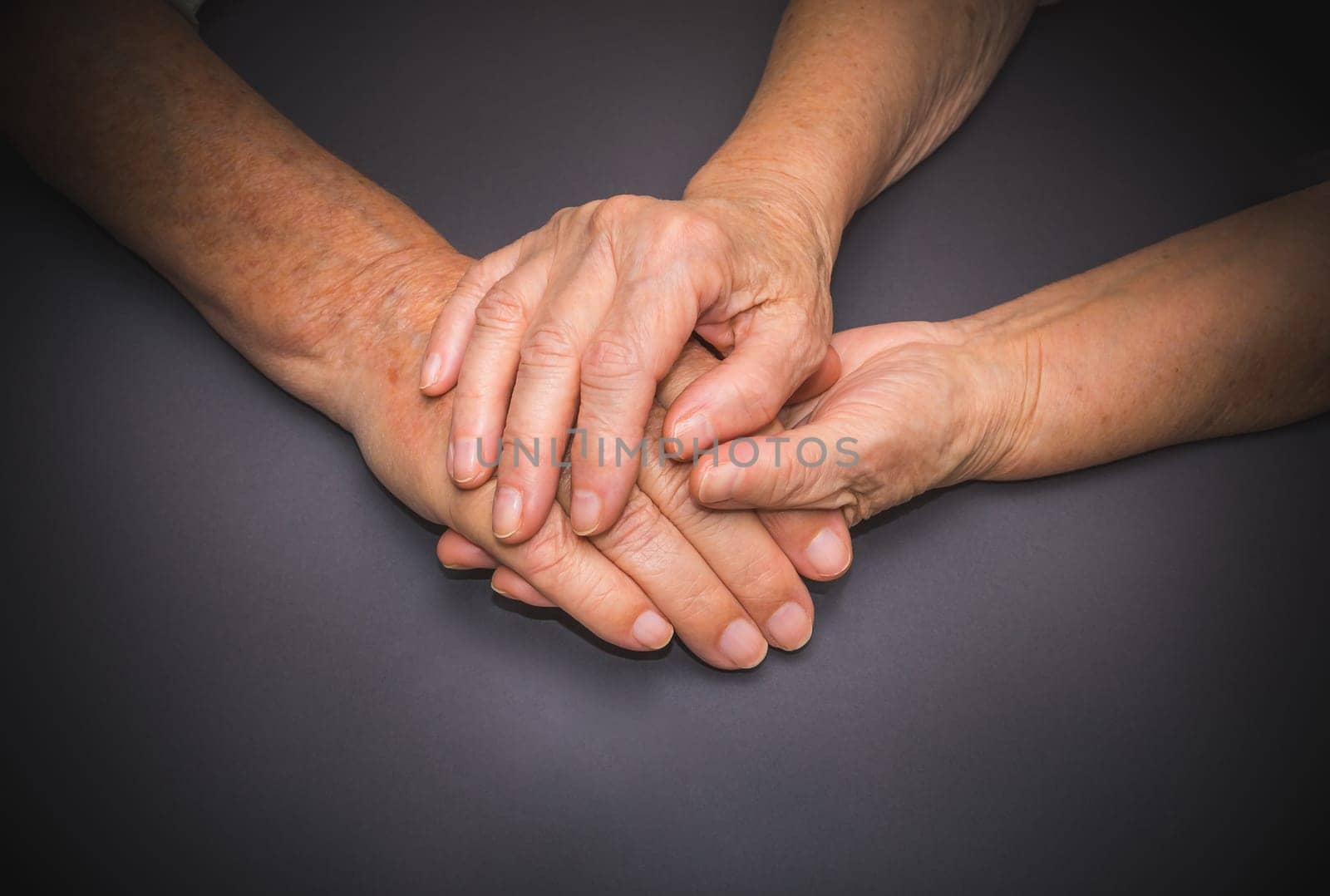 Hands of two loving senior people on a gray dark background