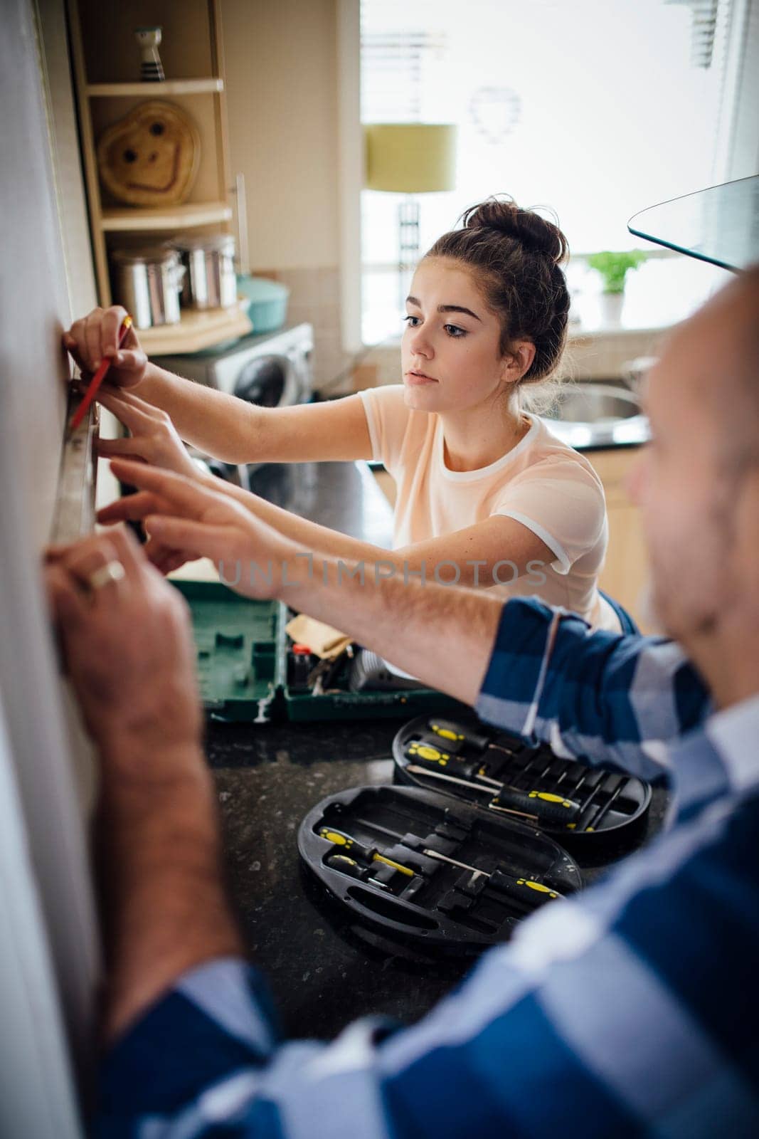 Teenage girl helping her father with DIy in their kitchen. The girl is marking the wall with a pencil.