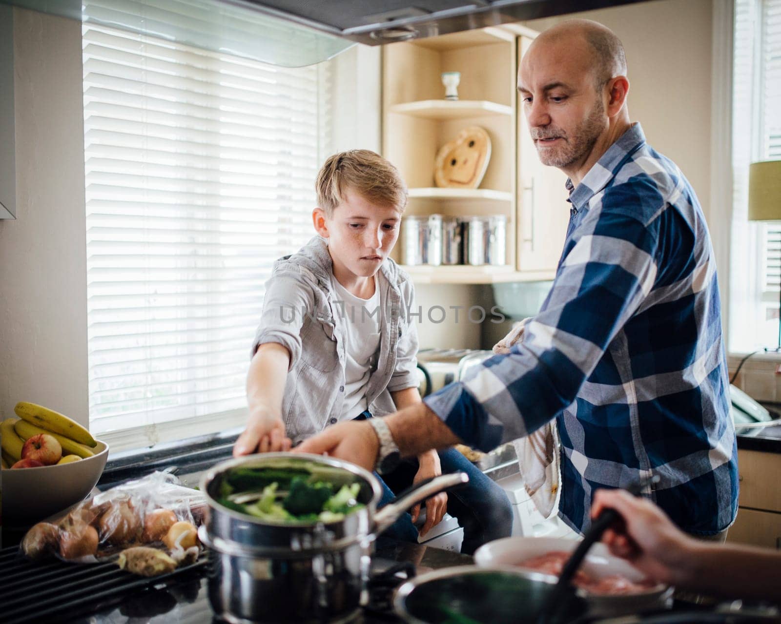 Father and son cooking dinner together in the kitchen. They are cooking vegetables on the hob.