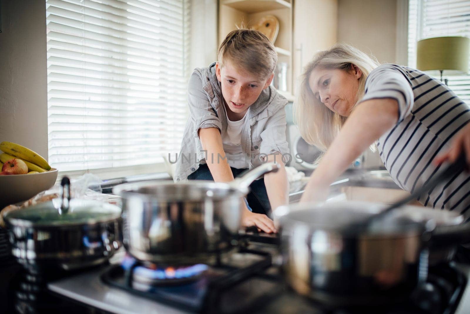 Mother and son cooking dinner together in the kitchen. They are cooking vegetables on the hob.