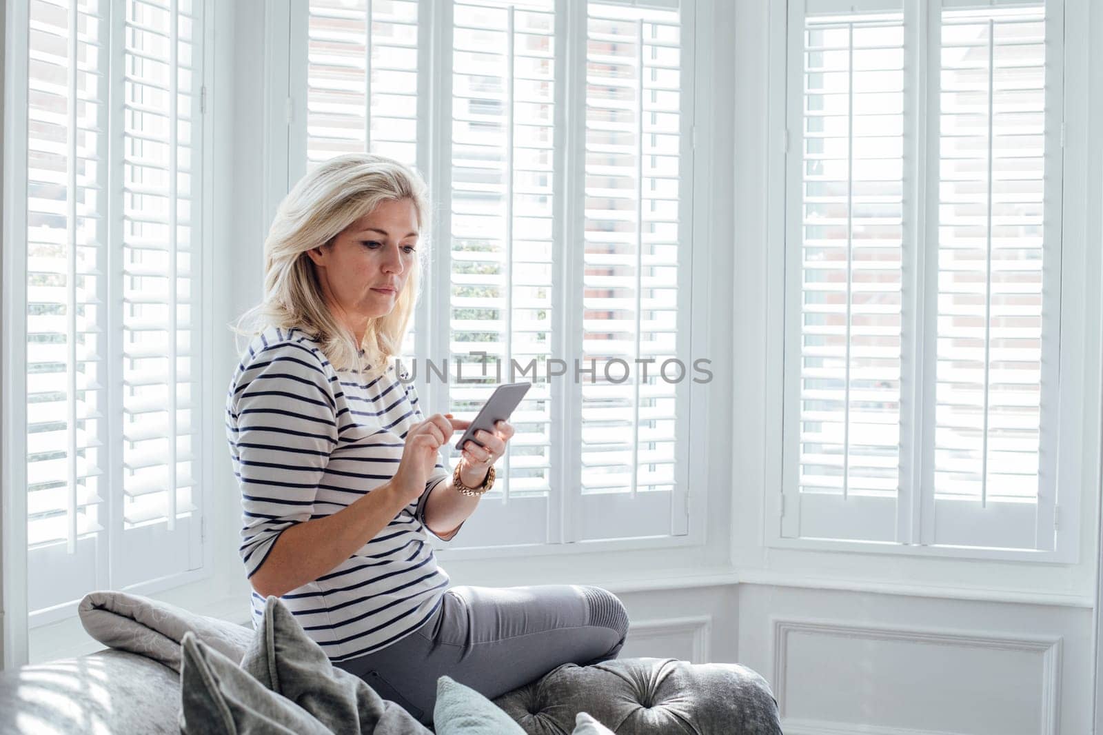 Mature woman using a smart phone. She is sitting on the sofa in her living room.