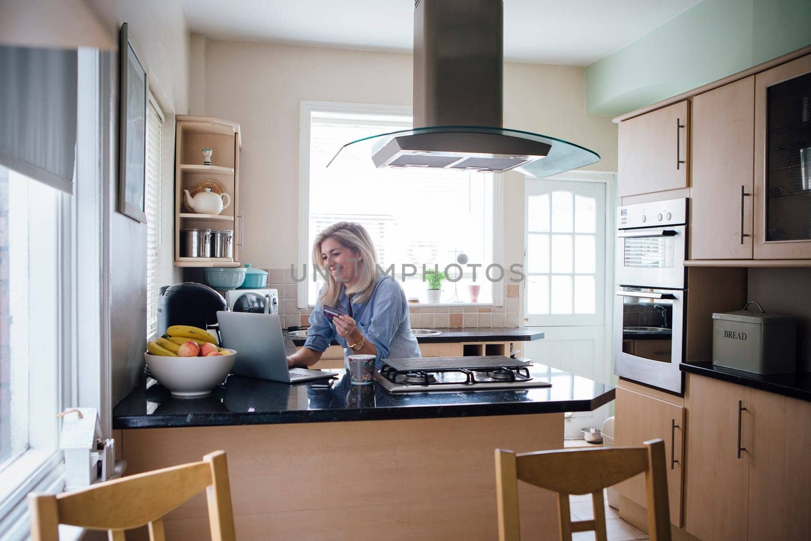 Mature woman using her laptop in her kitchen to make an online payment with a credit card.