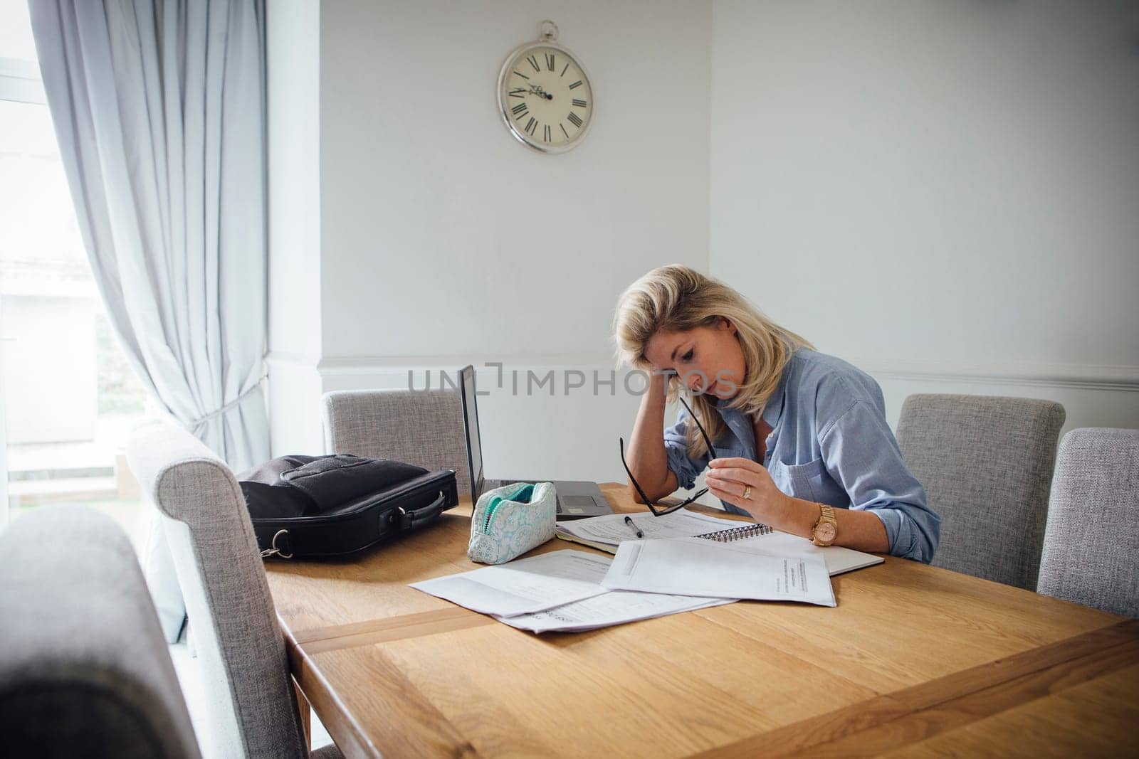 Mature woman working from home. She is sitting at the dining table with a laptop and paperwork.