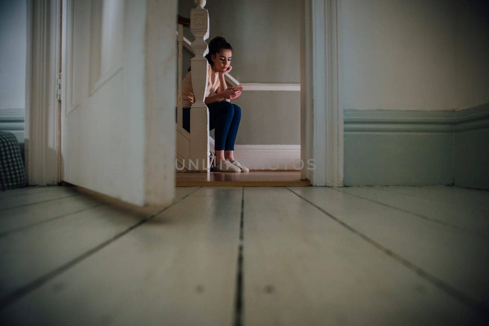 Teenage girl sitting at the bottom of a staircase using a smartphone.