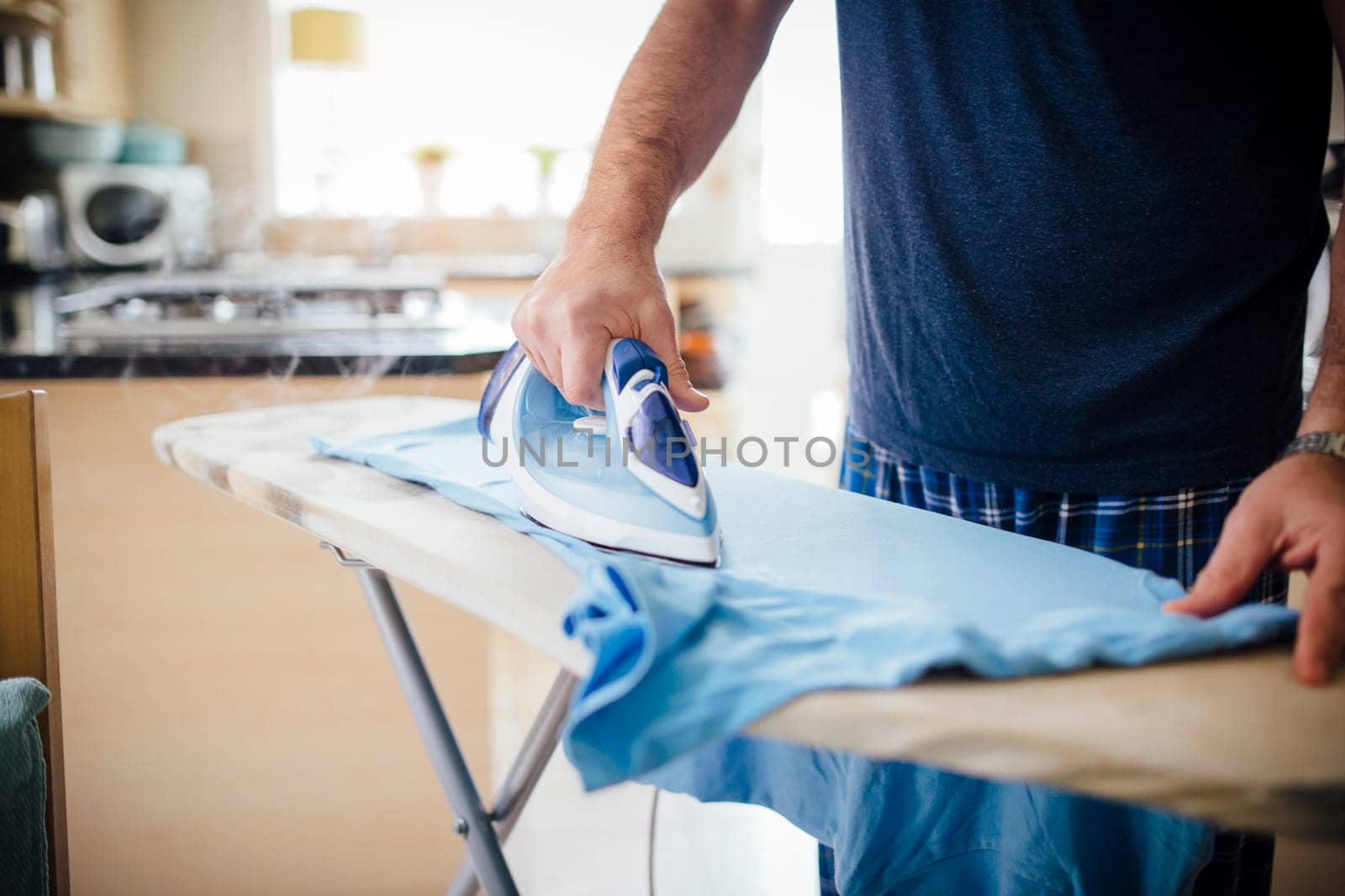 Close up of a mature man ironing a t-shirt in the kitchen.