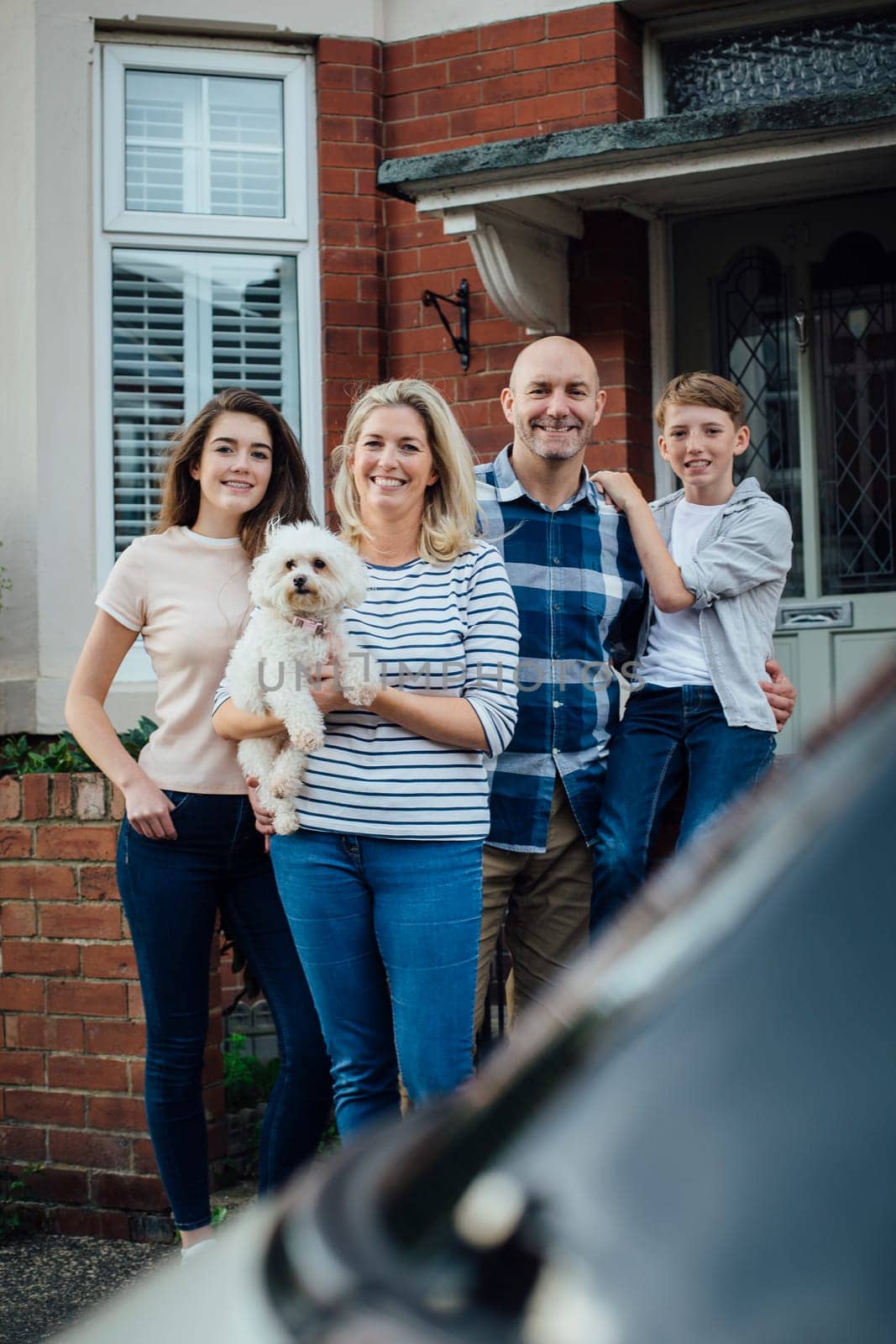 Family standing outside their home together with their pet dog, smiling for the camera.