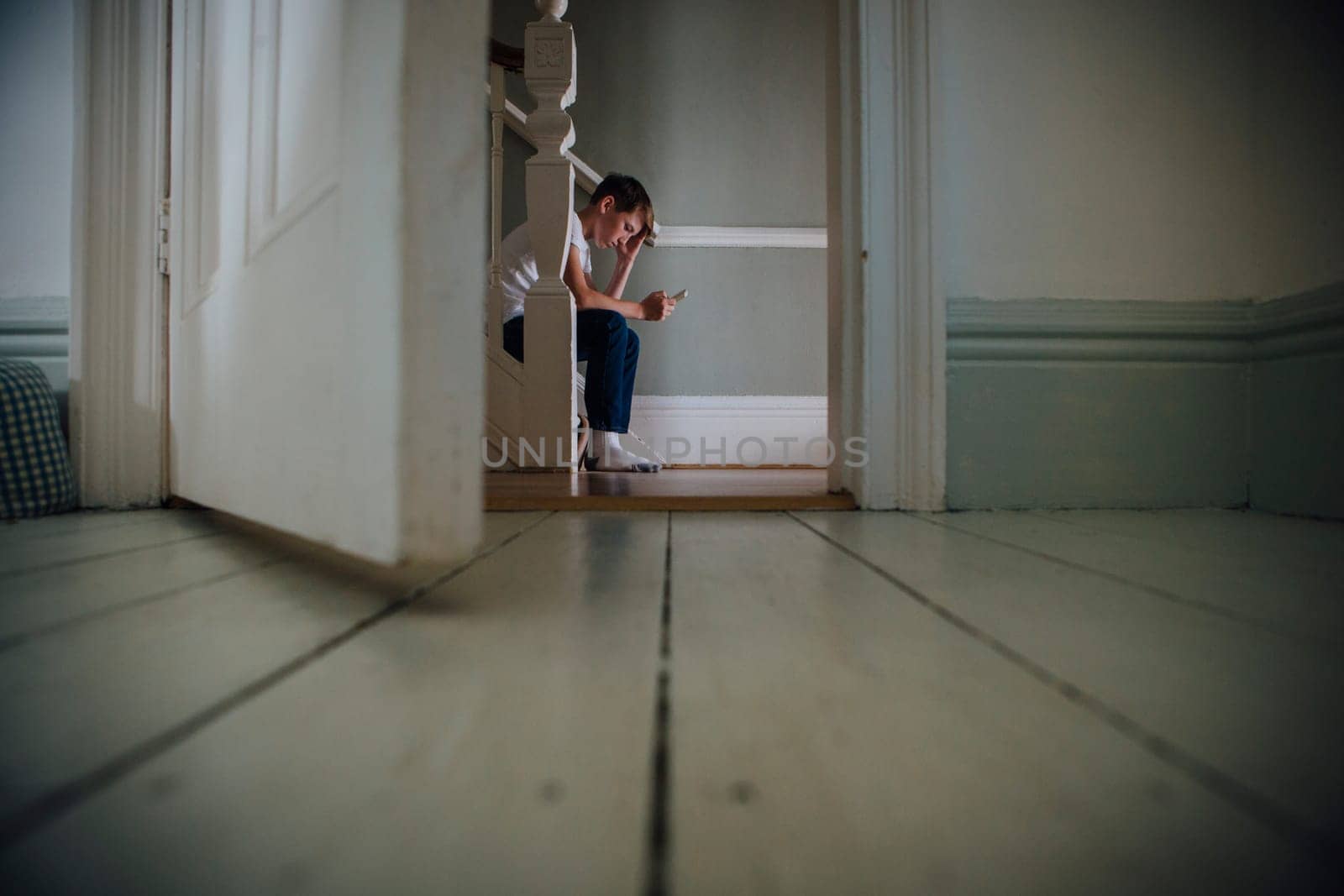 Boy sitting at the bottom of the stairs using a smartphone.