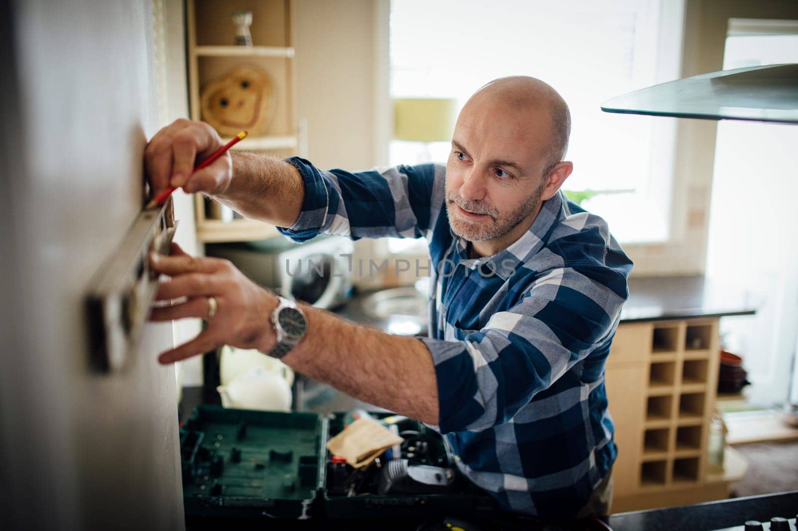 Mature man using a spirit level and marking the wall with a pencil in his kitchen.