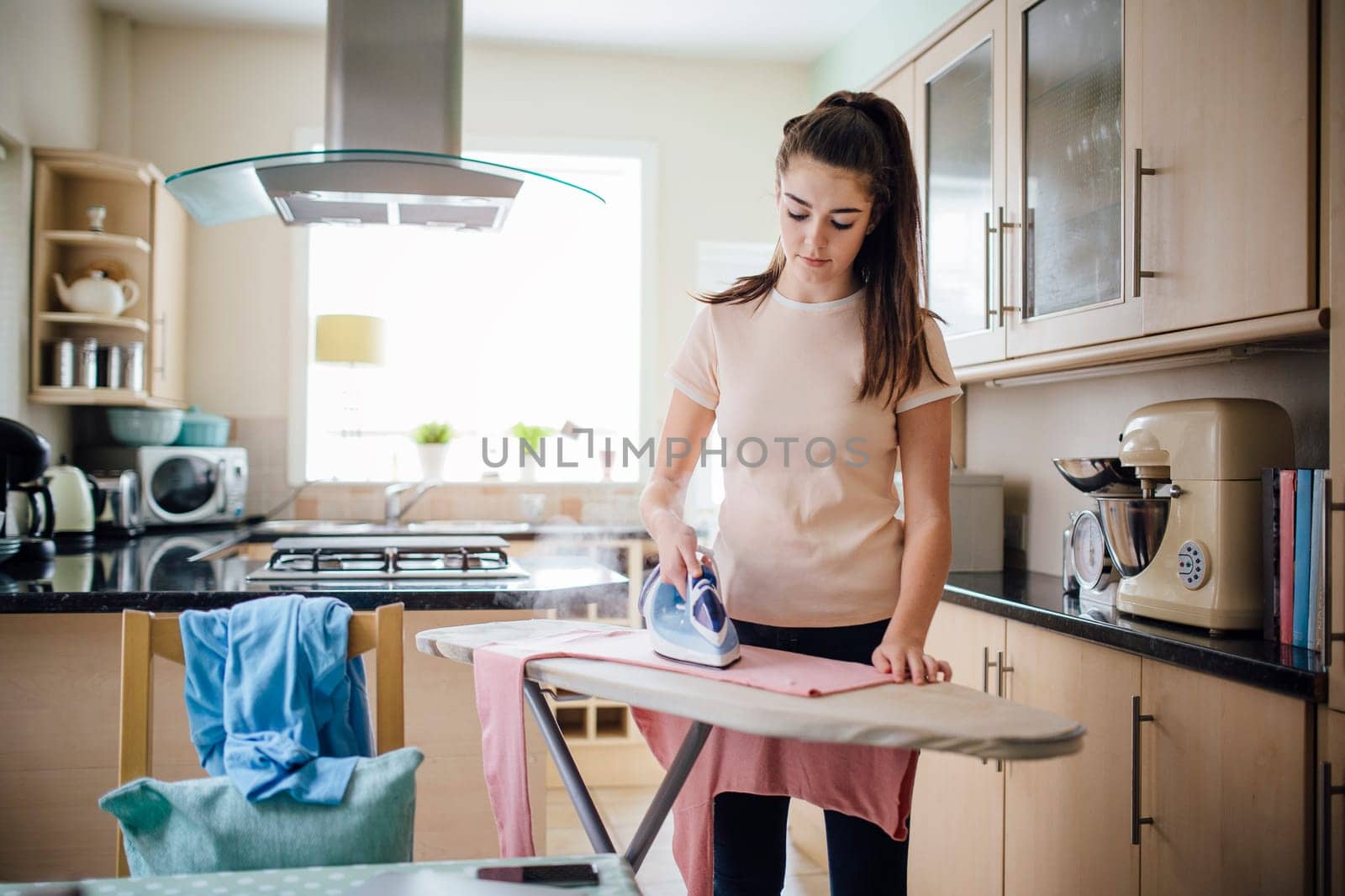 Teenage girl ironing laundry in the kitchen.