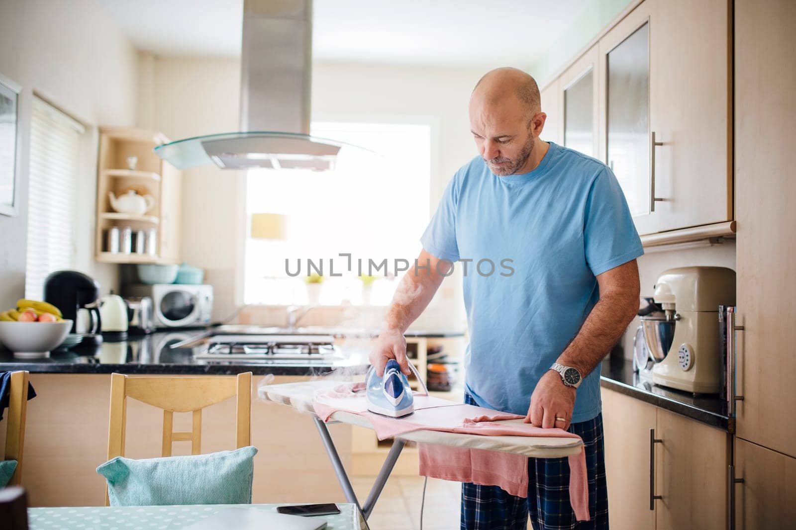 Mature man ironing laundry in the kitchen.