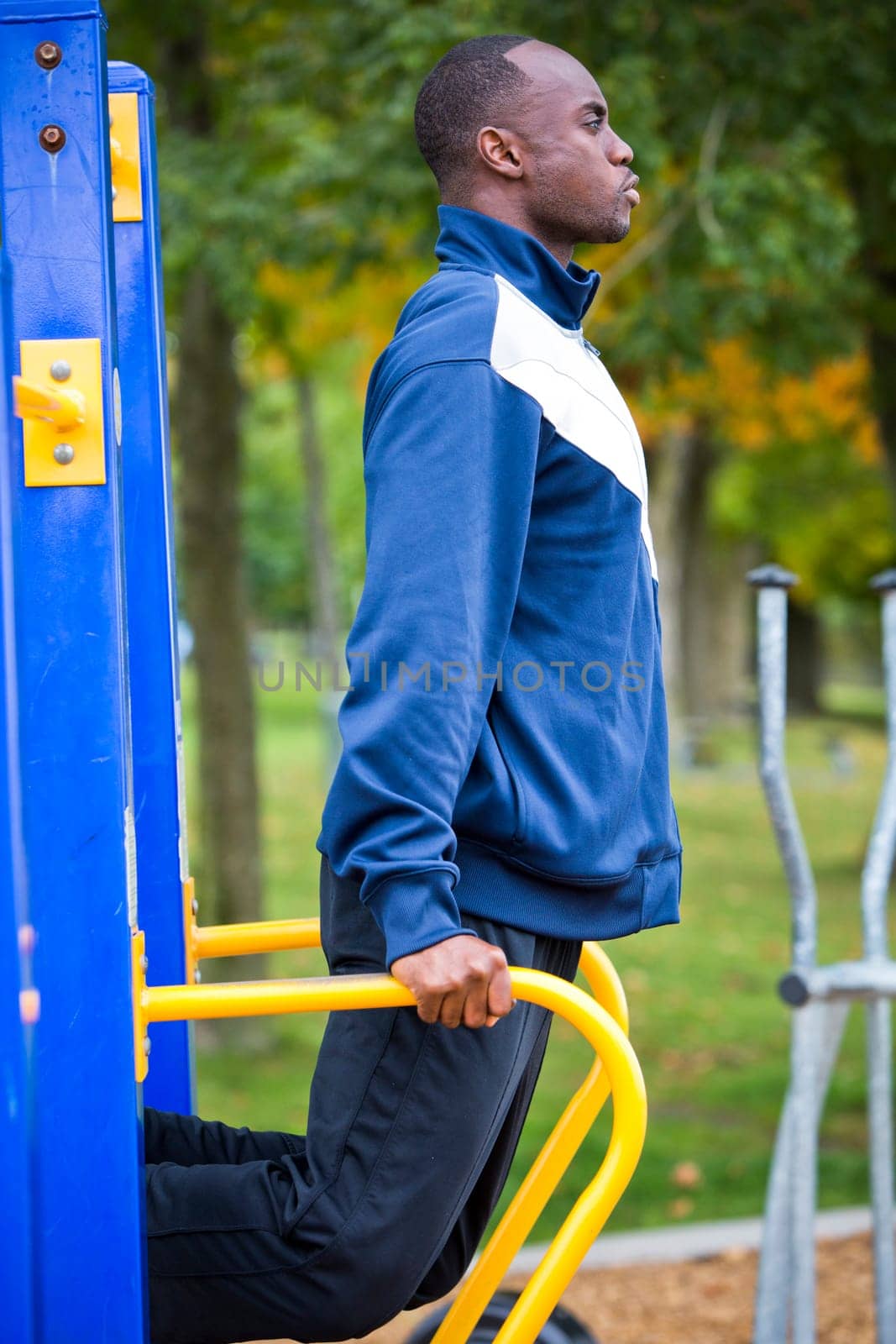 Active black man in training suit exercising at outdoor gym