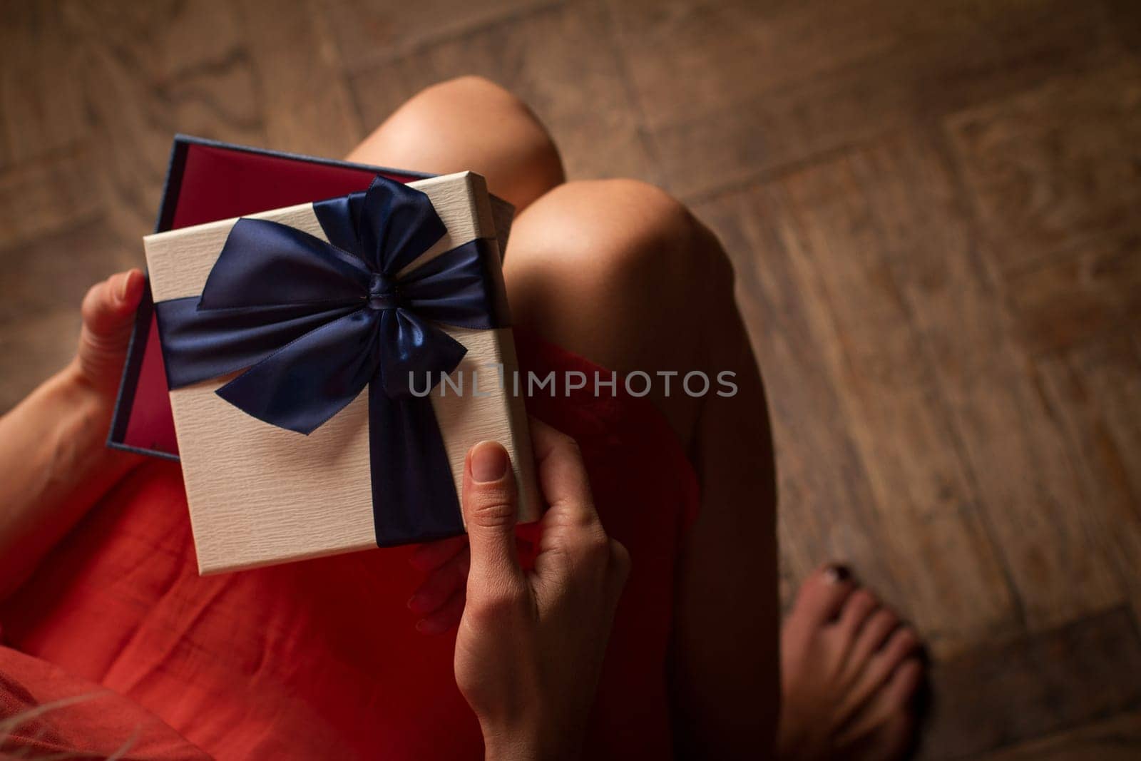 Top view woman opening a present with blue ribbon with three gift boxes inside on her knees