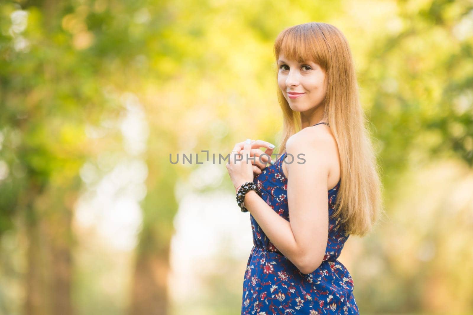 Beautiful young girl turned and looked up with a smile in the frame on the background of the sunny blurred greenery