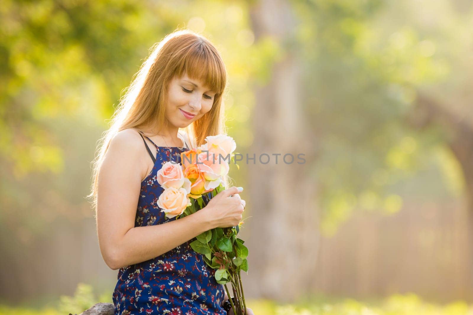 Beautiful young sexy girl looks at a bouquet of roses given to her standing against a background of green sunny blurred