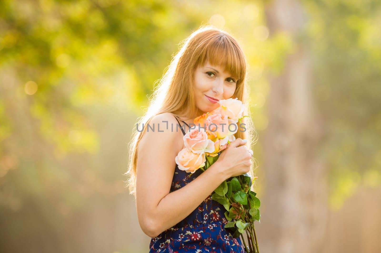 Beautiful young sexy girl standing with a bouquet of roses on a background of green sunny blurred