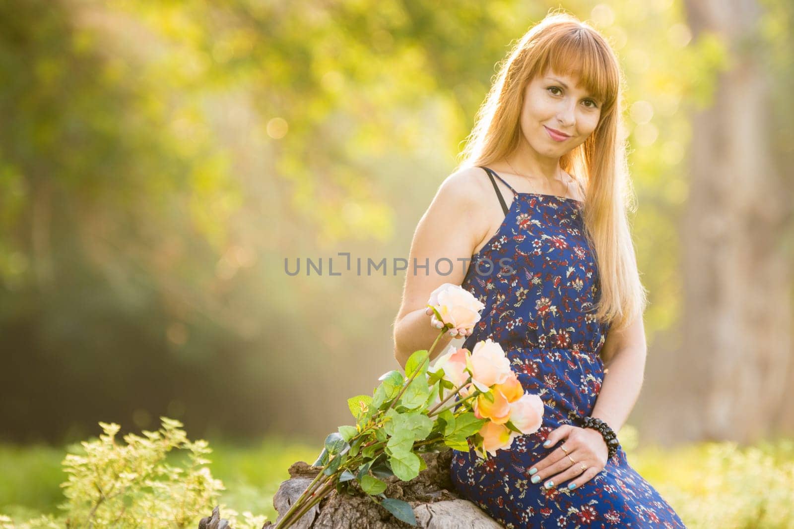 Beautiful young girl on the background of the sunny blurred greenery, lies next to a bouquet of roses