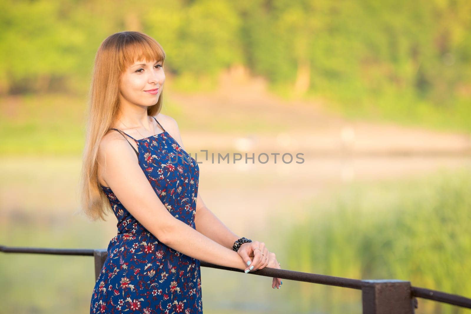 The charming young girl standing on a rustic bridge over the river at dawn sun