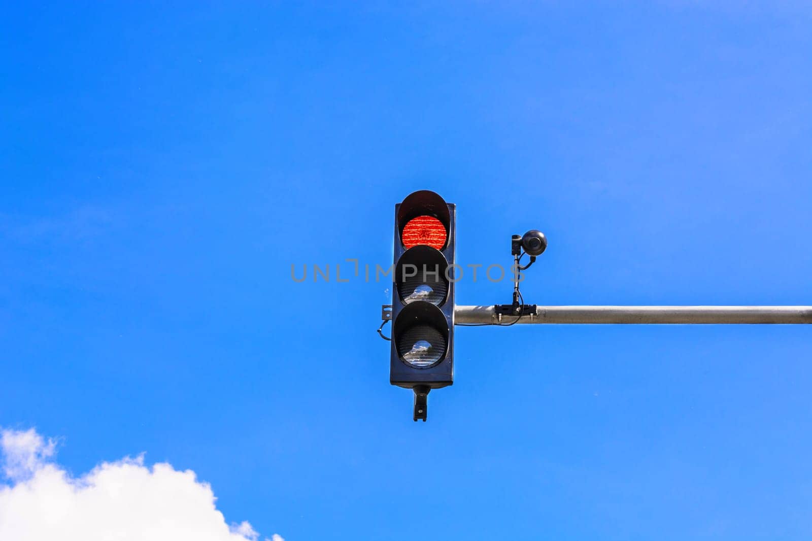 Traffic light and a security camera attached to a pole above the road.