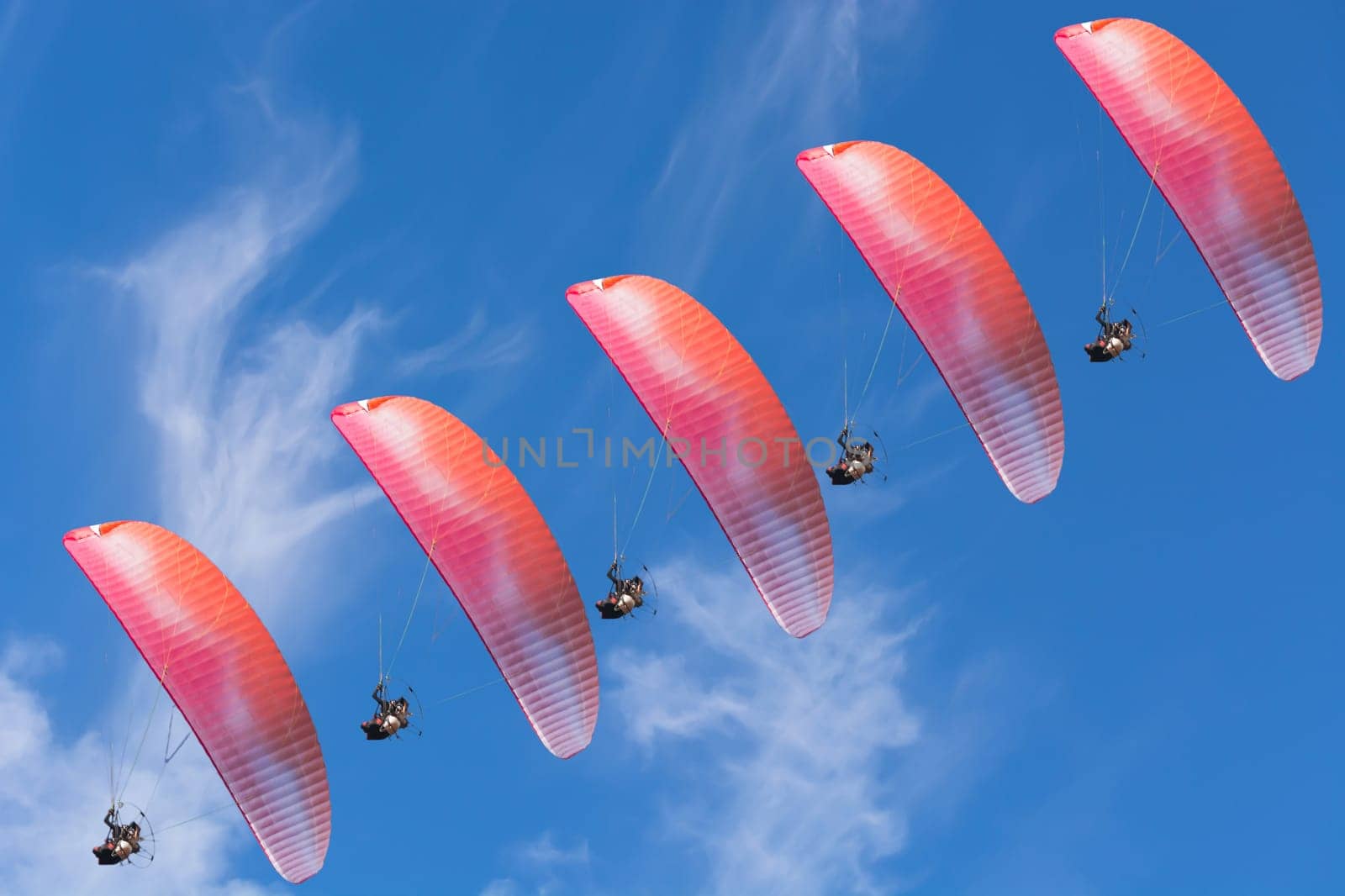 Five paragliders in a row in front of a blue sky..