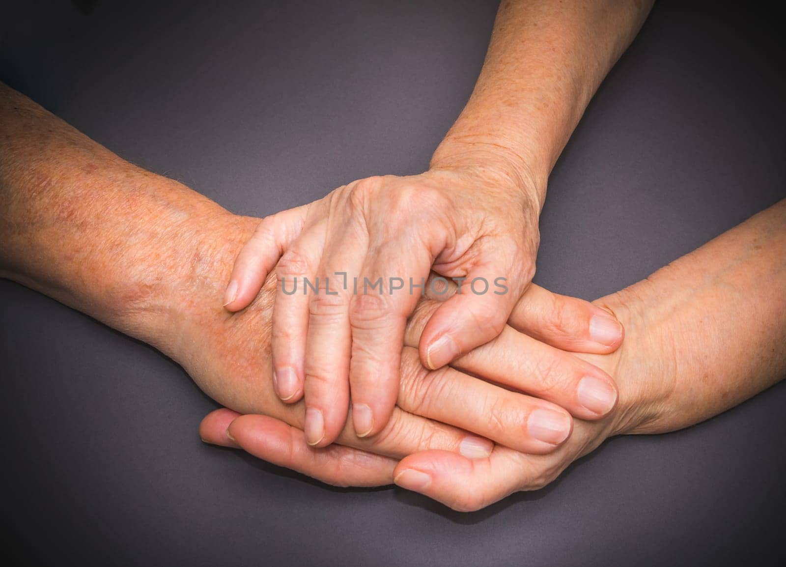 Hands of two loving senior people on a gray dark background
