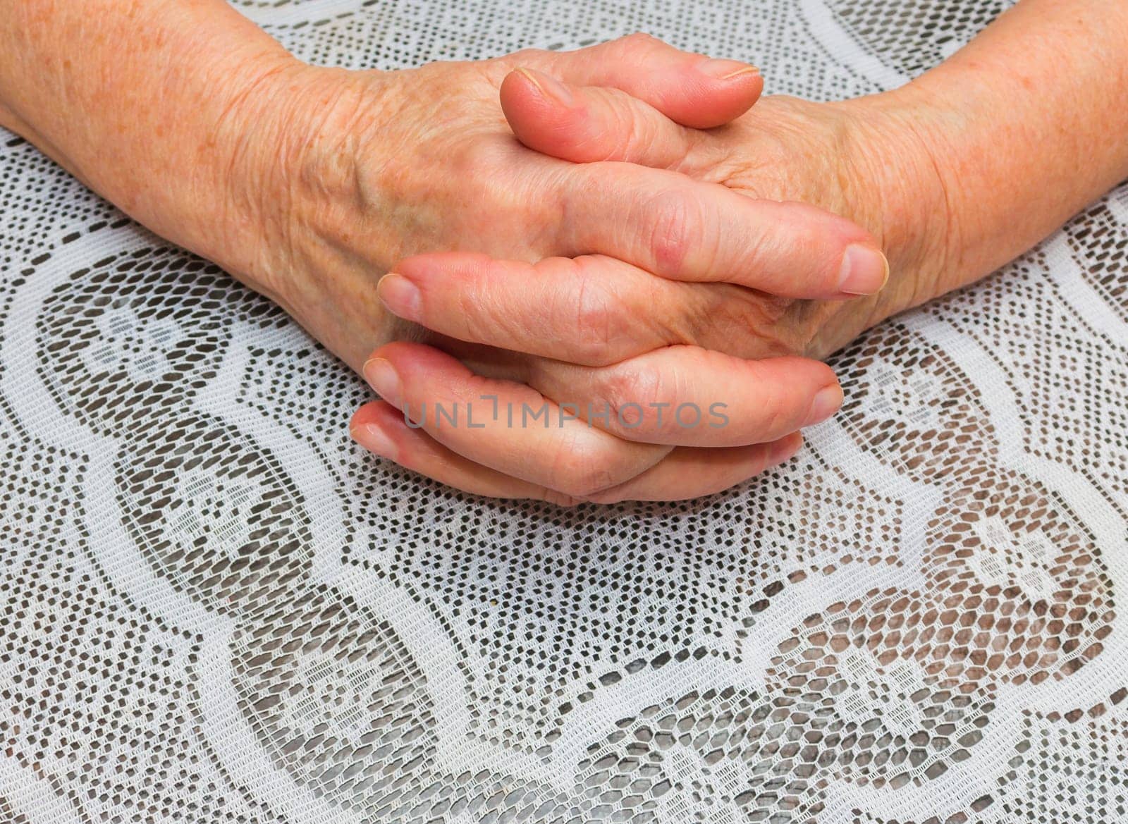 Hands of senior woman on a old tablecloth background