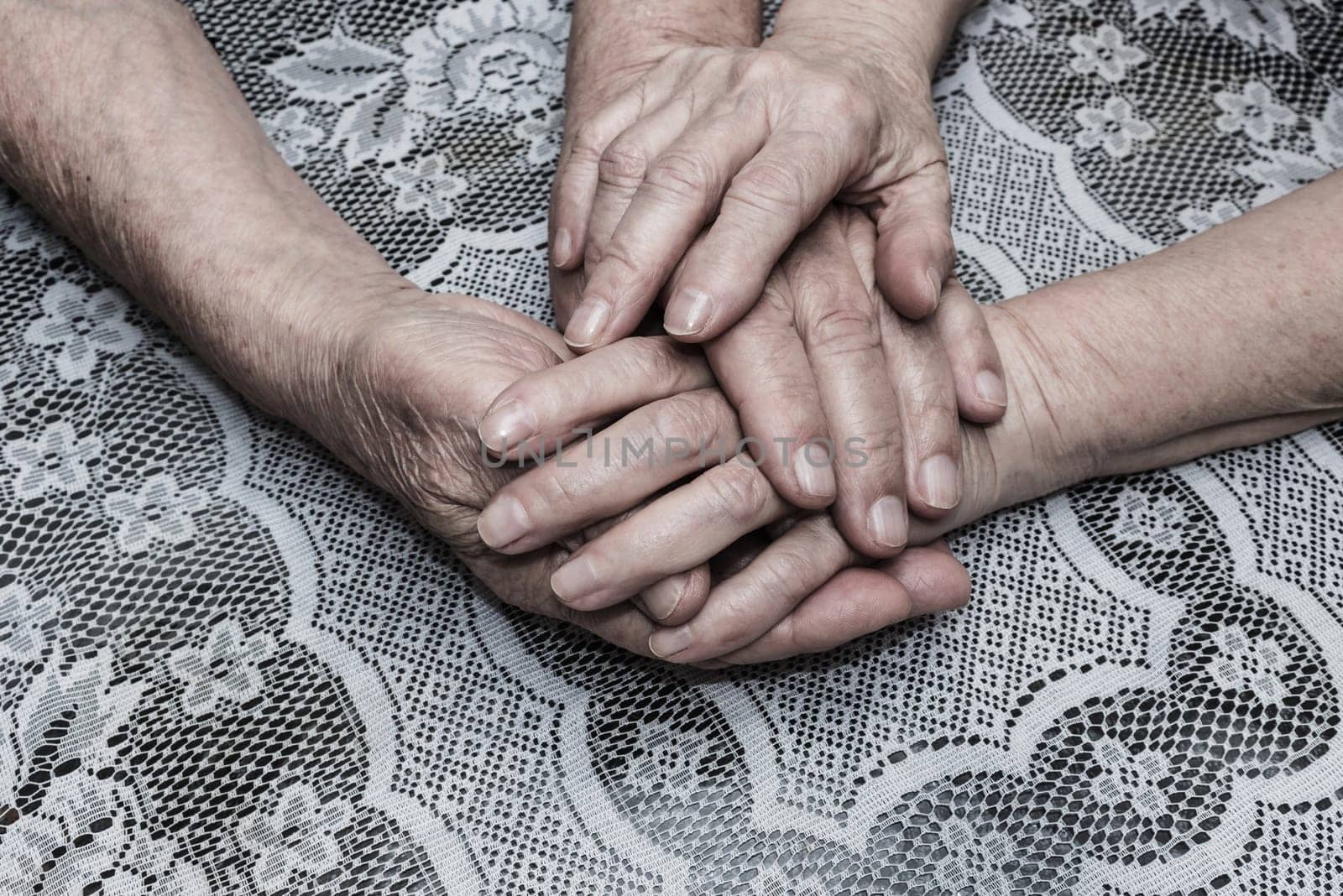 Hands of two loving senior people on a old tablecloth background
