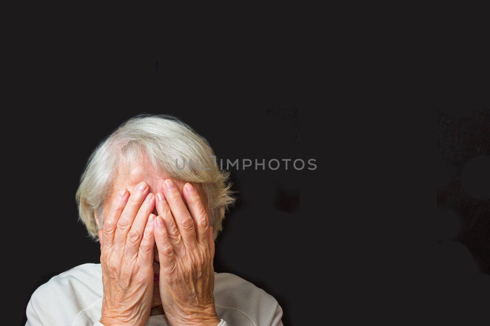 Portrait of an elderly woman with face closed by hands on black