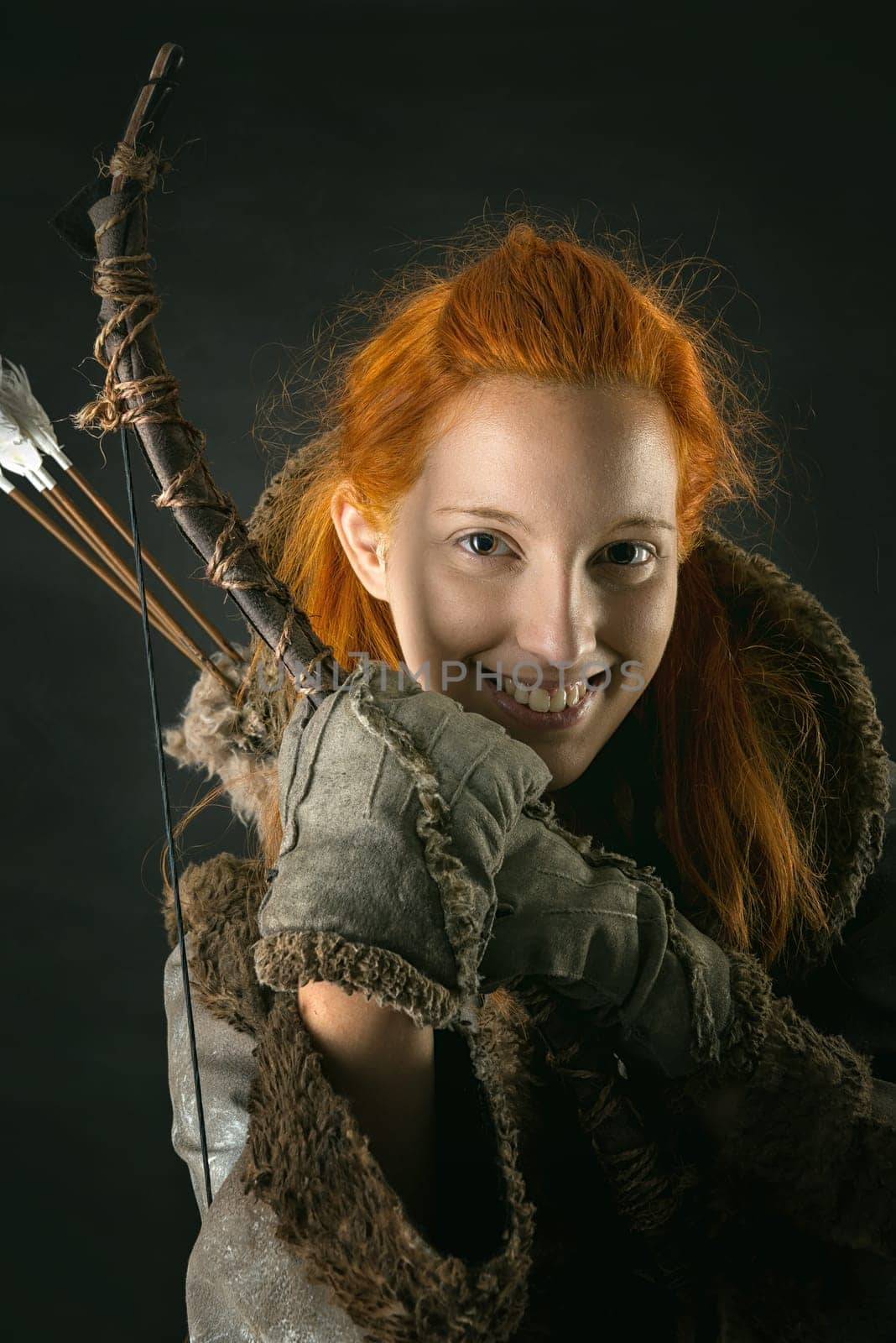girl archer in a costume with bow isolated in a dark background