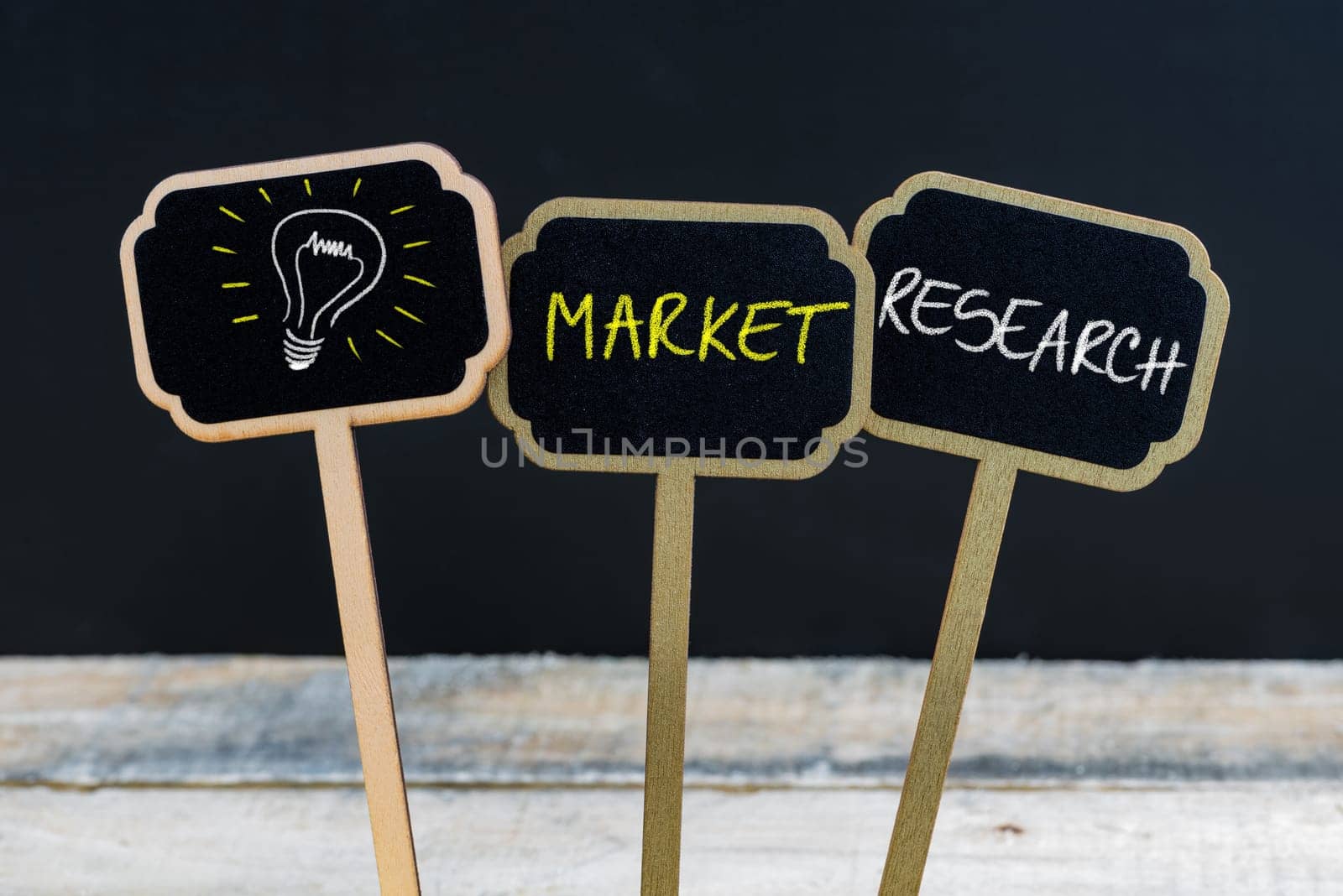 Concept message MARKET RESEARCH and light bulb as symbol for idea written with chalk on wooden mini blackboard labels, defocused chalkboard and wood table in background