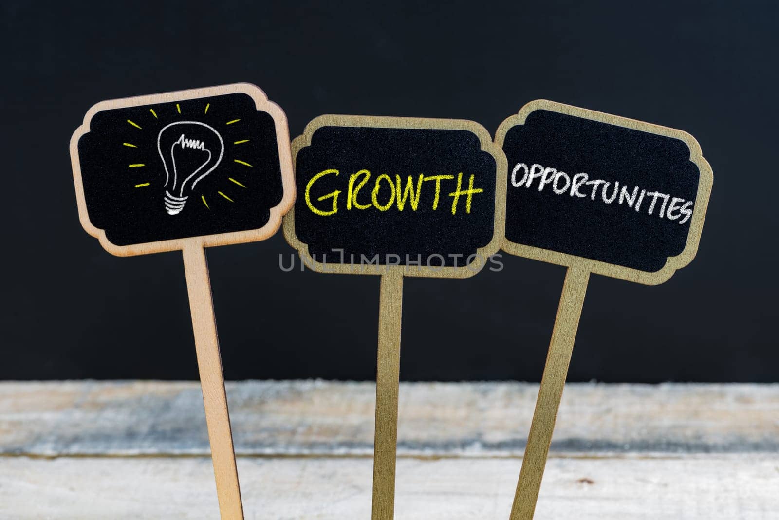 Concept message GROWTH OPPORTUNITIES and light bulb as symbol for idea written with chalk on wooden mini blackboard labels, defocused chalkboard and wood table in background