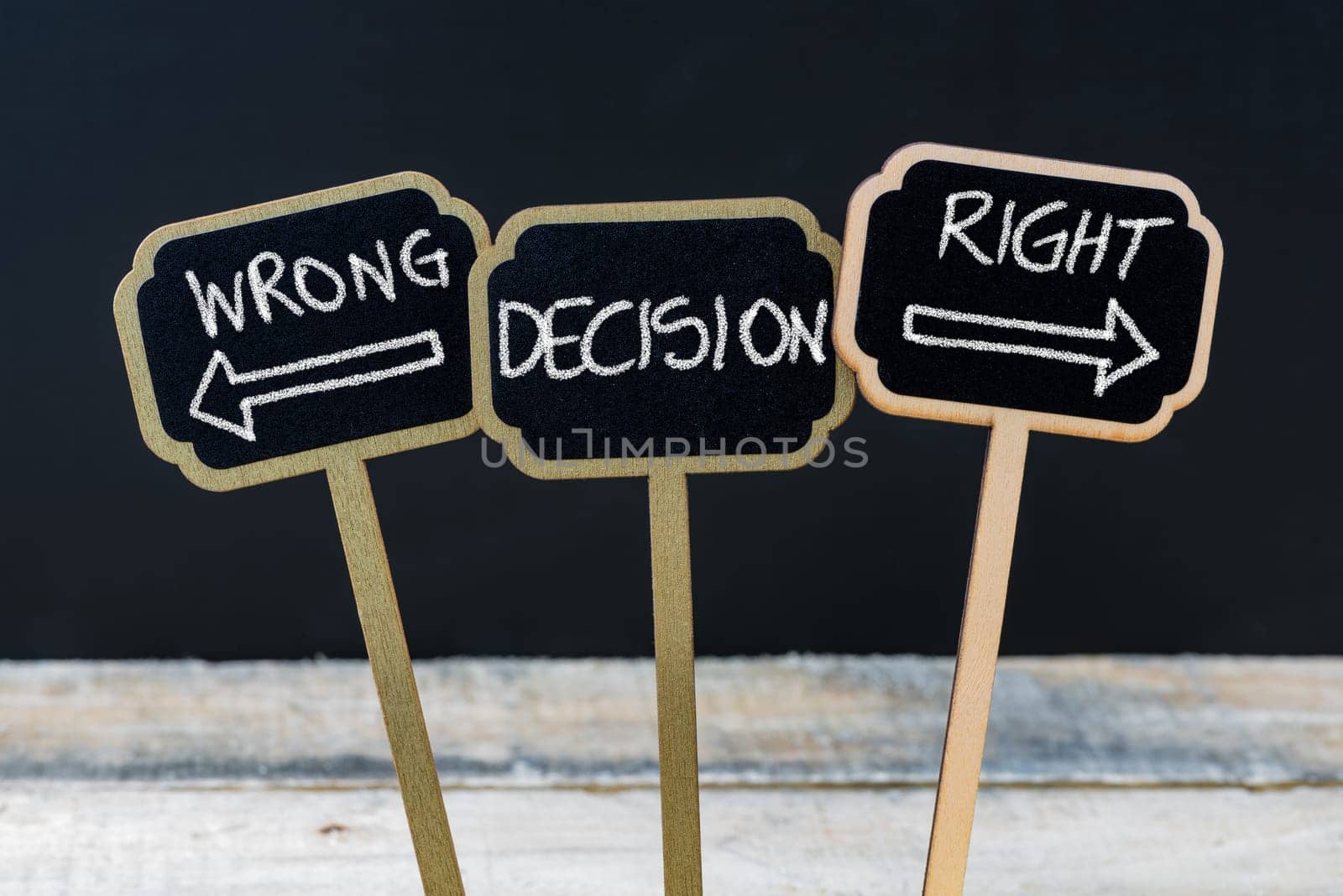 Concept message WRONG DECISION RIGHT DECISION written with chalk on wooden mini blackboard labels, defocused chalkboard and wood table in background
