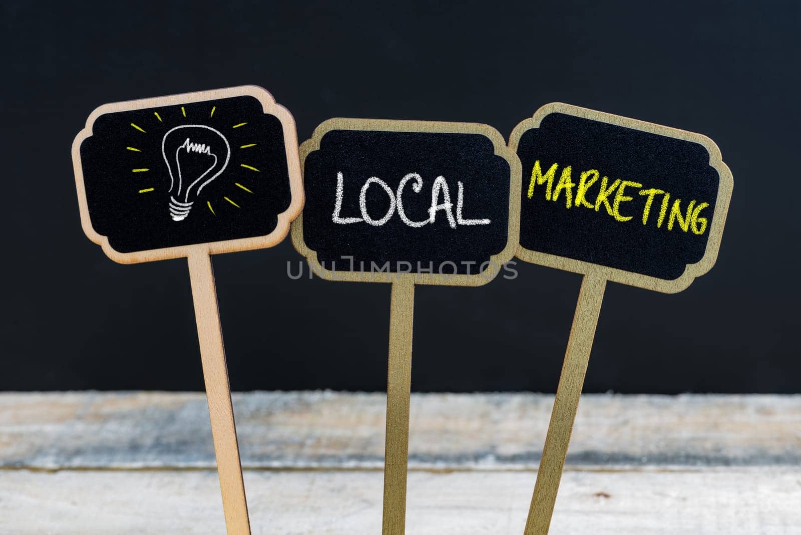 Concept message LOCAL MARKETING and light bulb as symbol for idea written with chalk on wooden mini blackboard labels, defocused chalkboard and wood table in background