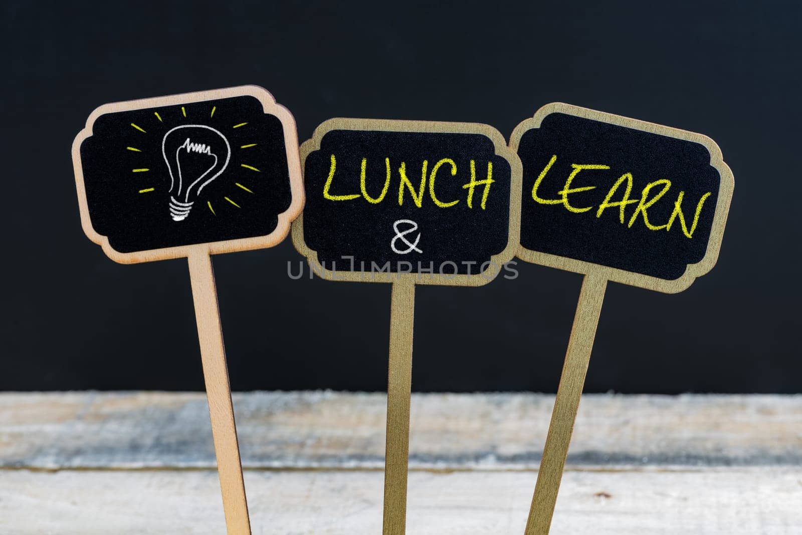 Concept message LUNCH and LEARN and light bulb as symbol for idea written with chalk on wooden mini blackboard labels, defocused chalkboard and wood table in background