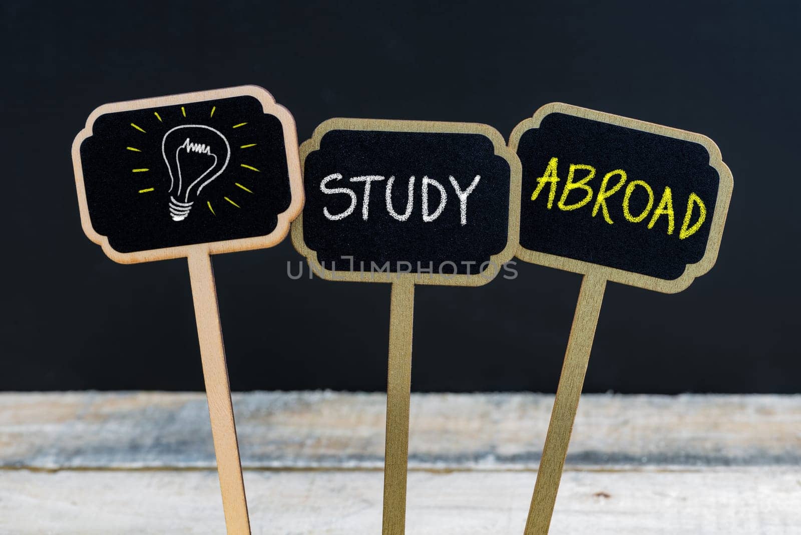 Concept message STUDY ABROAD and light bulb as symbol for idea written with chalk on wooden mini blackboard labels, defocused chalkboard and wood table in background