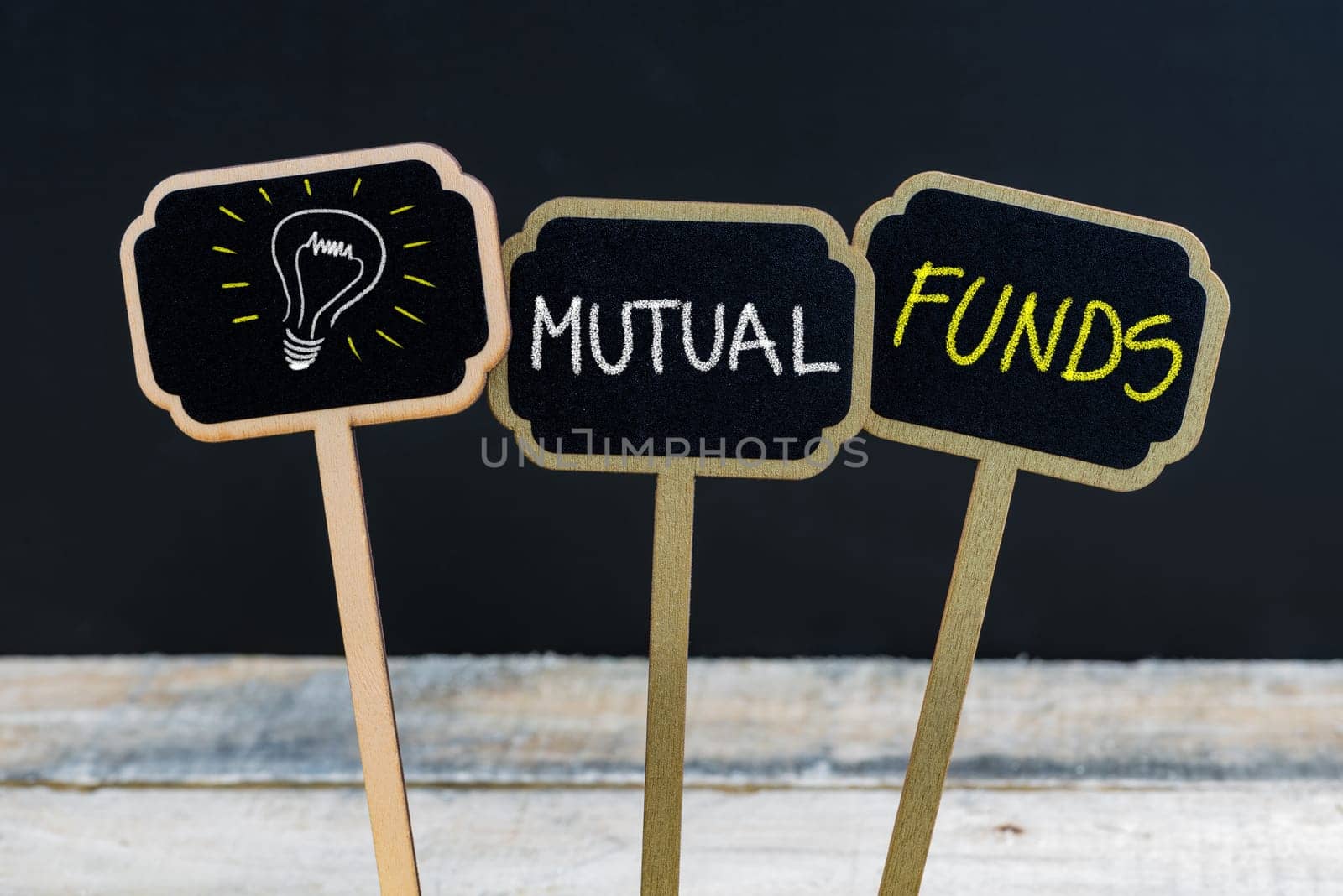 Concept message MUTUAL FUNDS and light bulb as symbol for idea written with chalk on wooden mini blackboard labels, defocused chalkboard and wood table in background