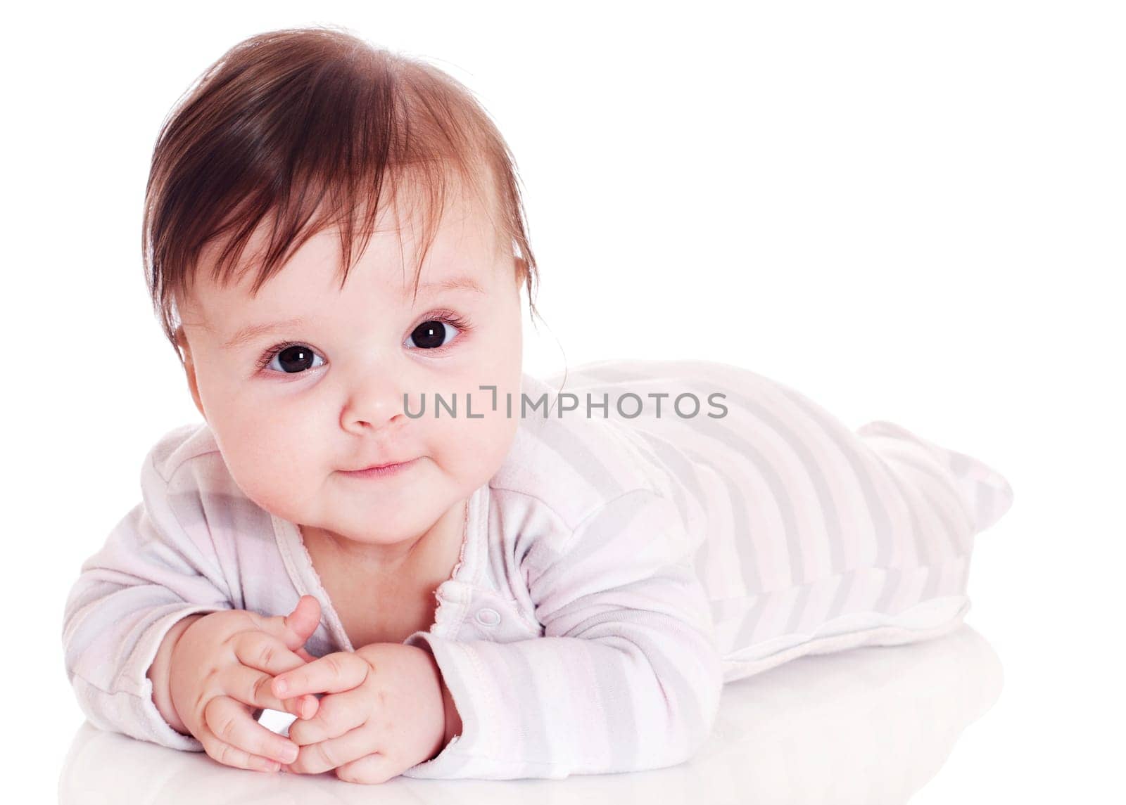 Happy baby lying on stomach on white floor background, wearing a cap and smiling big.