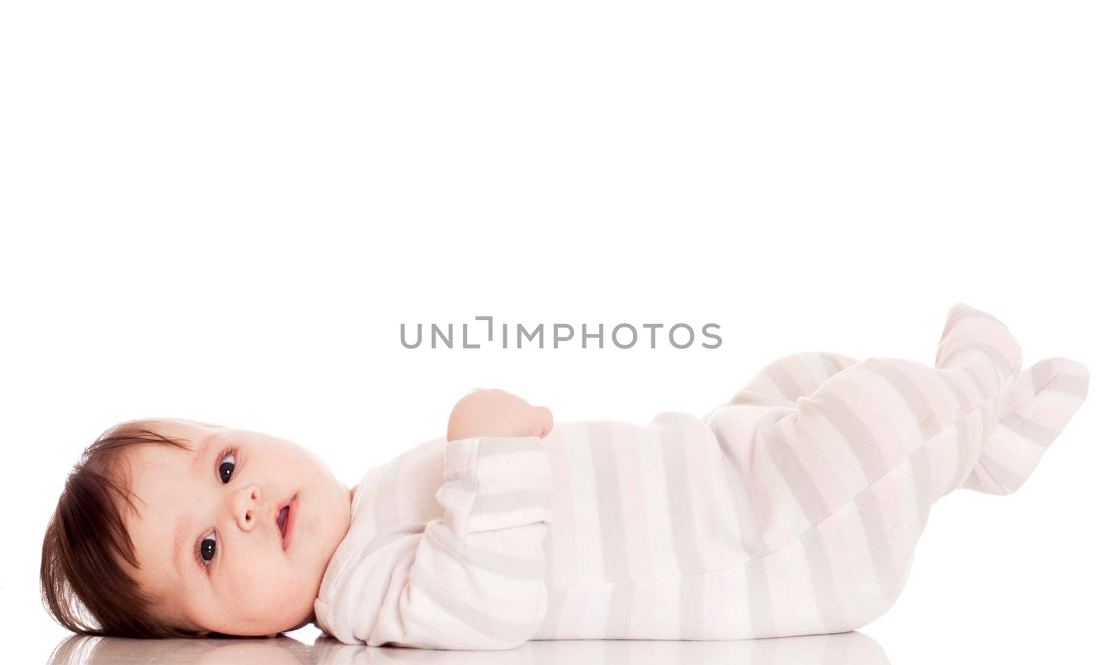 Happy baby lying on stomach on white floor background, wearing a cap and smiling big.