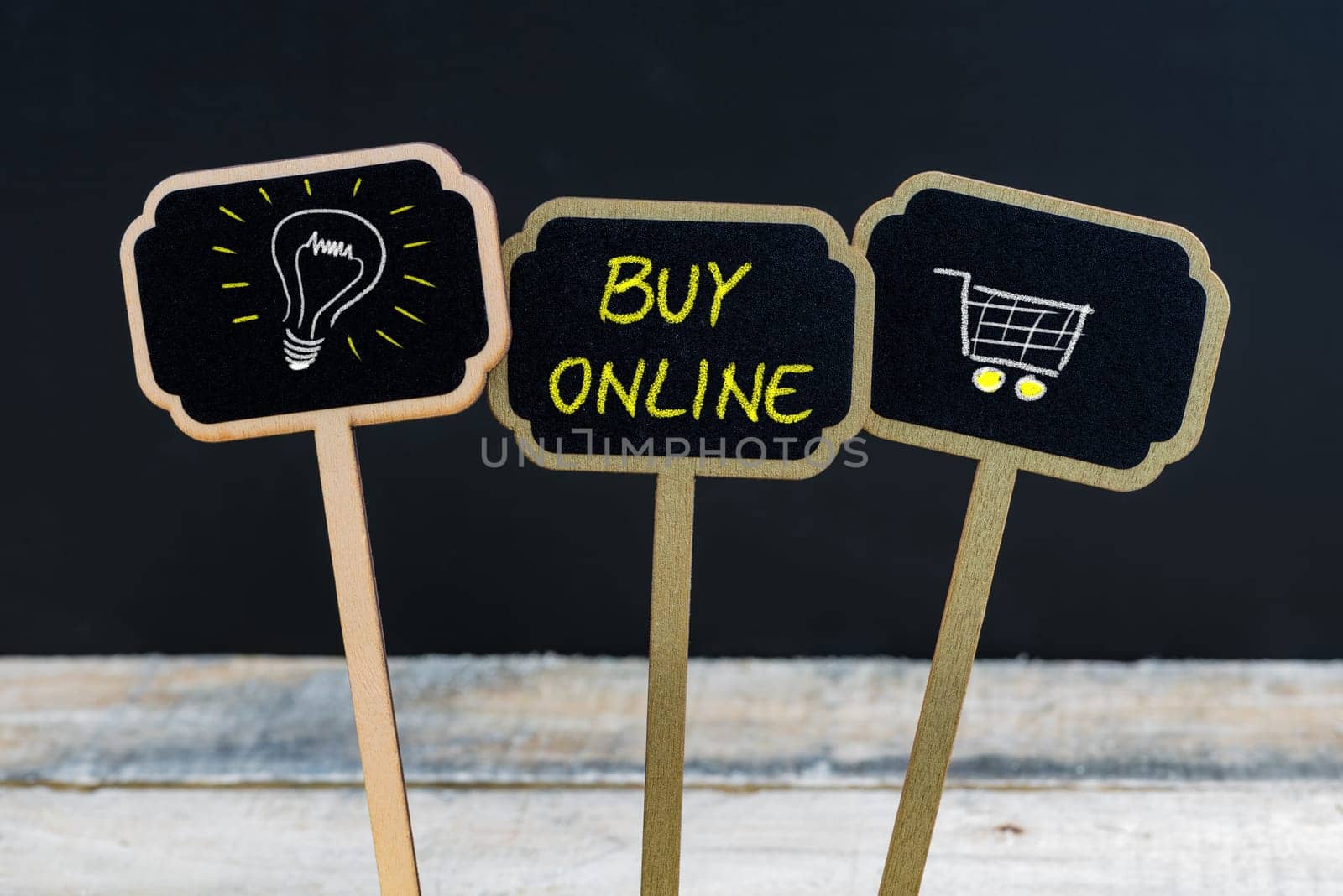 Concept message BUY ONLINE and light bulb as symbol for idea written with chalk on wooden mini blackboard labels, defocused chalkboard and wood table in background
