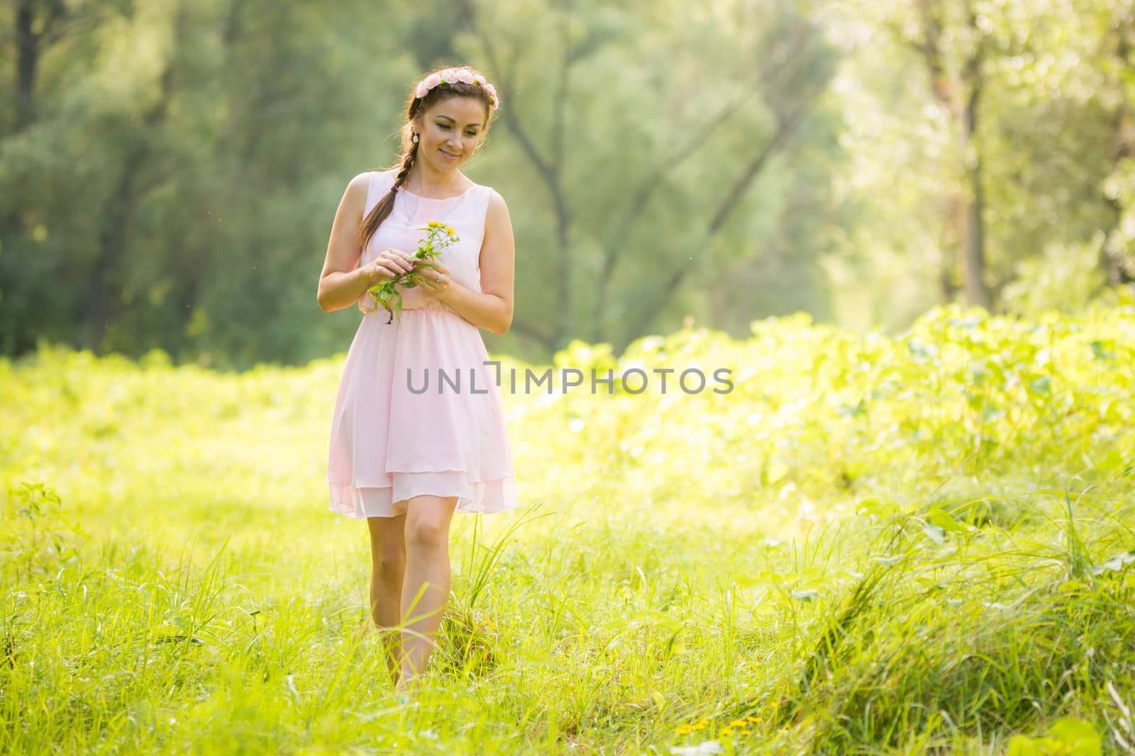 Young girl in the summer light dress collecting wild flowers